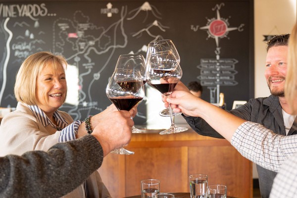 Smiling St. Innocent Winery guests raising their wine glasses at a table in the tasting Room